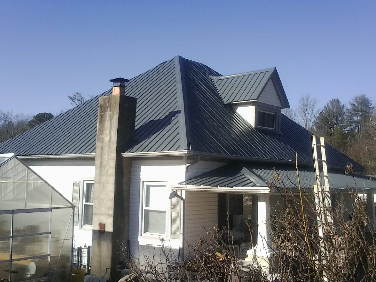 Dark blue standing seam metal roof on a white farmhouse with dormer — Slate & Tile Roof Repair by Roofing Brothers in Gray