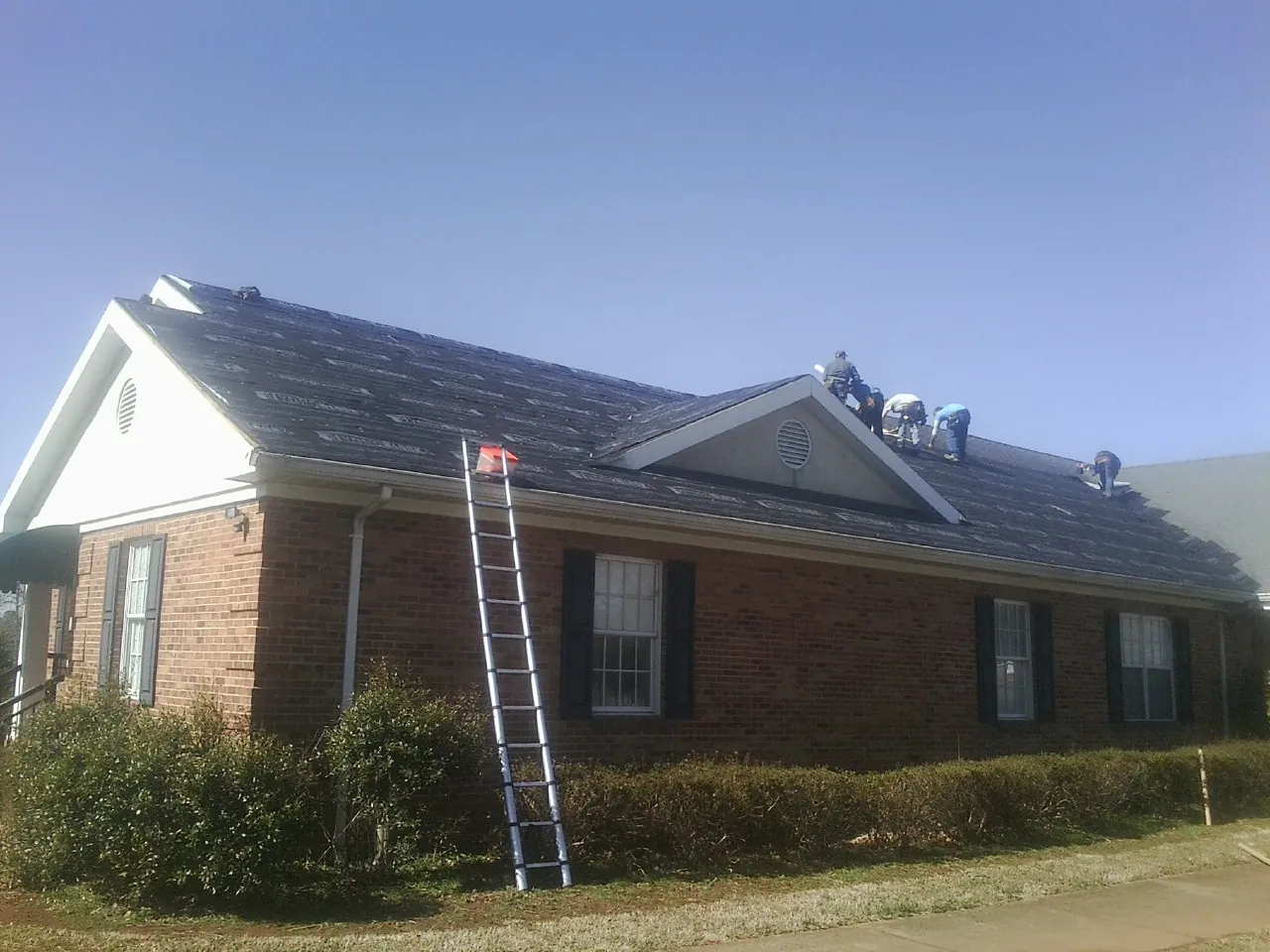 Crew tearing shingles off a brick ranch roof with a ladder set — Metal Roof Repair work by our crew in Gray