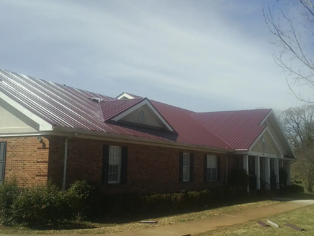 Red metal roof with gabled entries on a long brick building, from a Hail Damage Roof Repair job in Gray