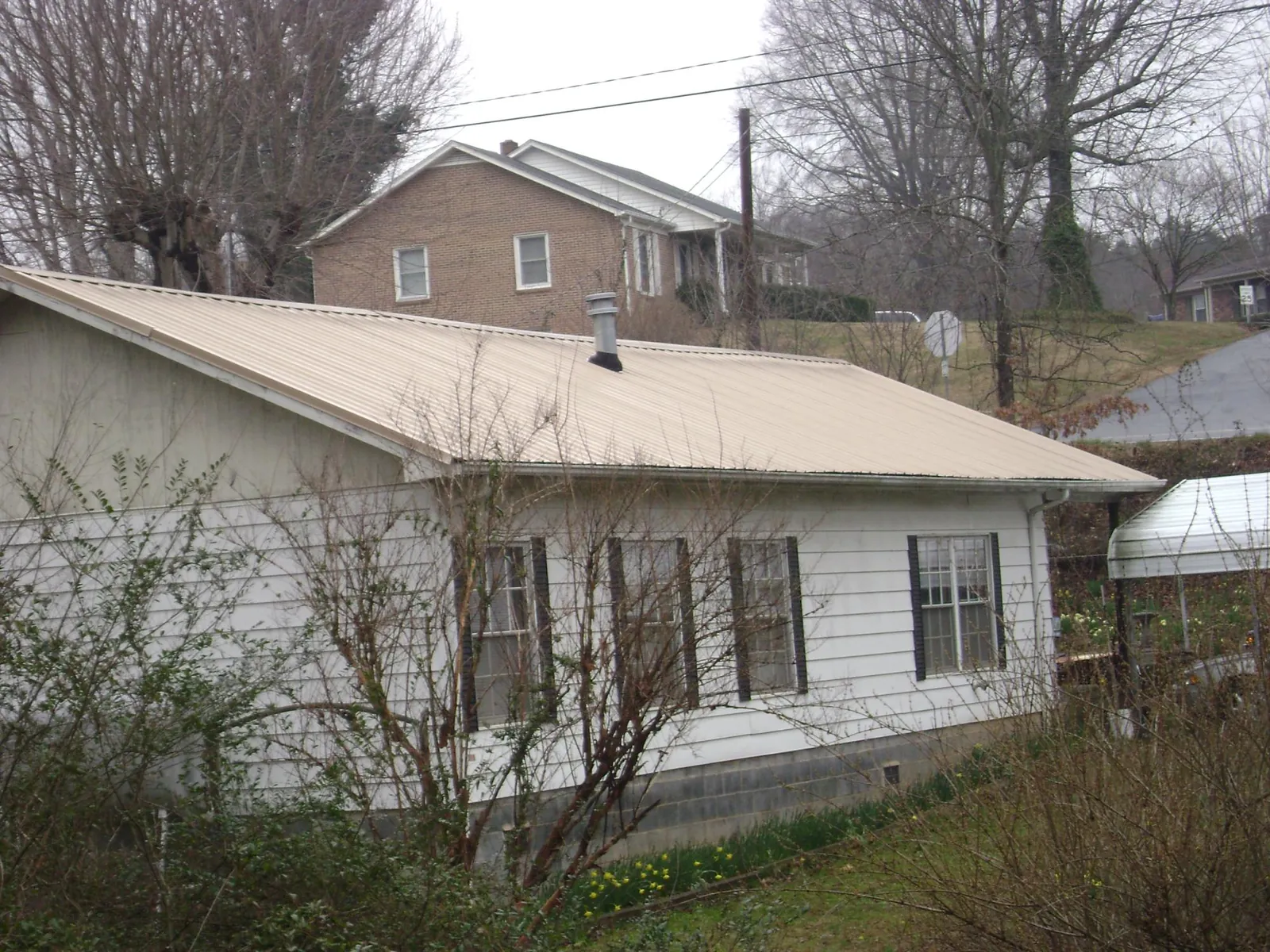 Tan metal roof on a white sided house set into a hillside — Commercial Roofing by Roofing Brothers in Gray